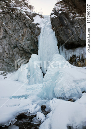 Frozen waterfall in winter mountain landscape. Ice formation on rock cliff 135290997