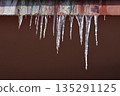 Icicles hanging from a red roof edge 135291125