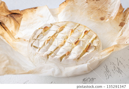 Baked camembert cheese with roasted garlic in rustic parchment wrap 135291347