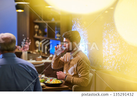 Muslim family enjoying iftar at a restaurant decorated for Ramadan with warm lighting and traditional ornaments Muslim family enjoying iftar at a restaurant decorated for Ramadan with warm lighting and traditional ornaments 135291432