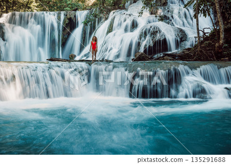 Woman in swimsuit standing on tropical waterfall, turquoise water, exotic nature and travel concept. Woman in swimsuit standing on tropical waterfall, turquoise water, exotic nature and travel concept. 135291688