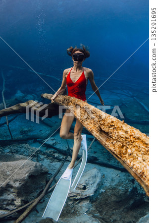 Woman freediver in red swimsuit exploring underwater lake with fins in clear blue freshwater Woman freediver in red swimsuit exploring underwater lake with fins in clear blue freshwater 135291695