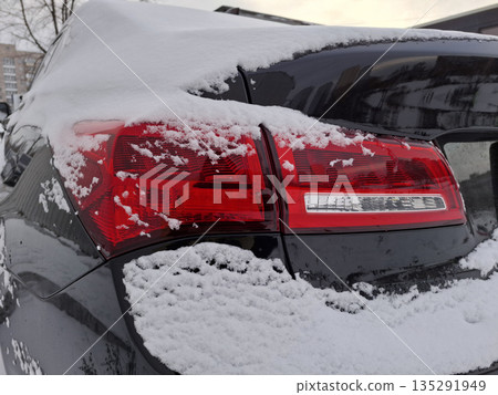 Rear red headlight of black car is covered in snow. White snow lies on black car Rear red headlight of black car is covered in snow. White snow lies on black car 135291949