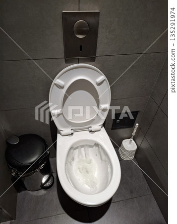 Restroom interior with white toilet. Water drains from toilet cistern Restroom interior with white toilet. Water drains from toilet cistern 135291974