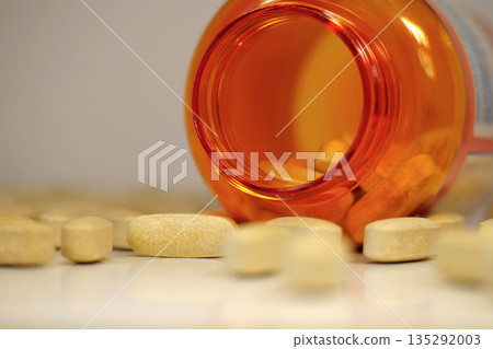 Big yellow pills and open orange jar on table. In reality these are vitamin C 135292003