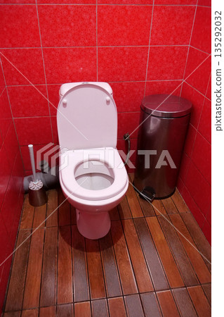 Toilet room with toilet bowl, wastebasket, toilet brush and red wall tiles 135292032