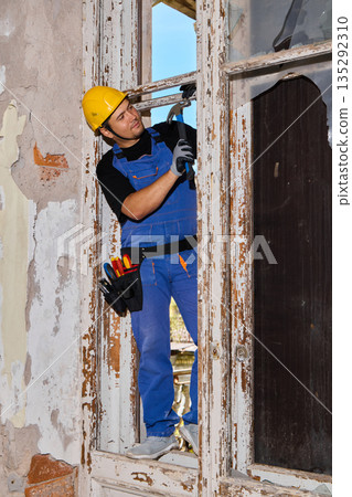 Window installer adjusting frame with spirit level on ladder Window installer adjusting frame with spirit level on ladder 135292310