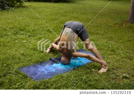 Person in deep forward bend relaxing on grassy park surface Person in deep forward bend relaxing on grassy park surface 135292319