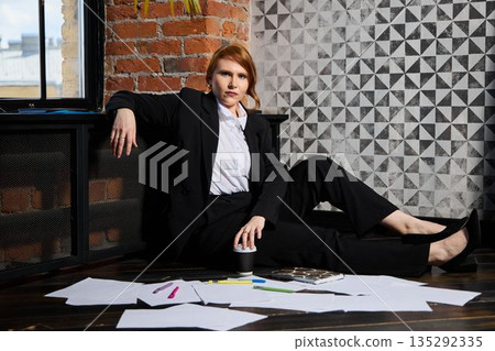 Caucasian creative director lounges among scattered papers in loft 135292335