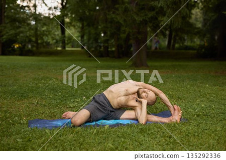 Individual executing deep side stretch on blue exercise mat outdoors 135292336