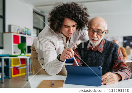 Senior man learning digital skills with tutor support in community center. Senior man learning digital skills with tutor support in community center. 135293358