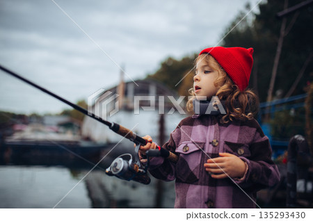 Child enjoying fishing outdoors during cold season. 135293430