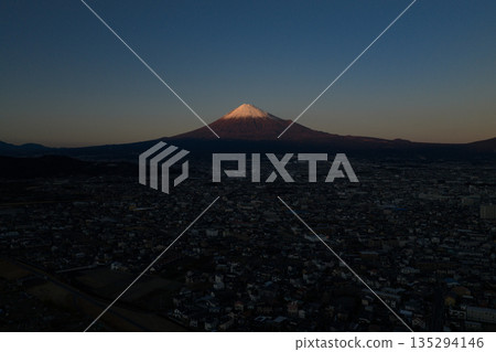 Mount Fuji and the cityscape of Fuji City at dusk as seen from the Fuji River riverbed (aerial view) 135294146