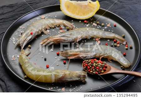 Raw shrimp with spices on a black round plate 135294495