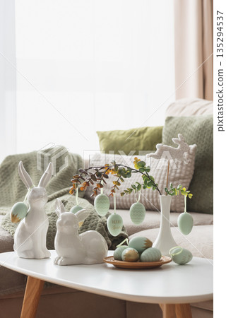 Cozy Easter Living Room Decor with Bunny Figurines and Hanging Eggs on White Table 135294537