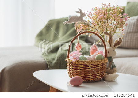 Easter Basket with Ester Eggs,  Plush Bunny and Spring Decor on White Table intoCozy Living Room 135294541