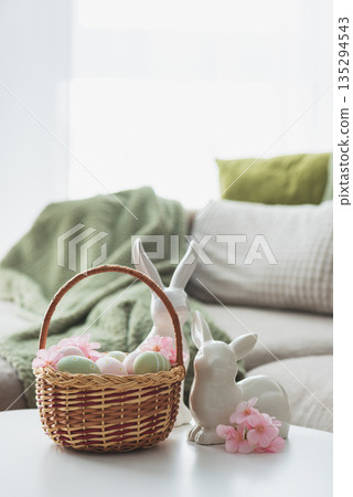 Easter Basket with Ester Eggs,  Plush Bunny and Spring Decor on White Table intoCozy Living Room 135294543