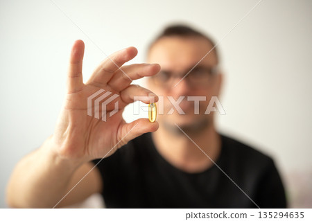 Man holding omega 3 soft gel capsule in his hand Man holding omega 3 soft gel capsule in his hand 135294635