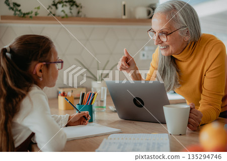 Grandmother helping granddaughter with homework or school project. 135294746