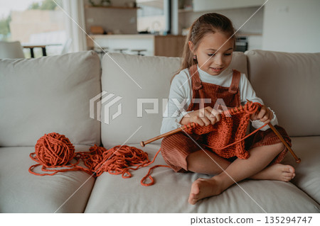 Little girl knitting at home on sofa, learning creative handcraft skills Little girl knitting at home on sofa, learning creative handcraft skills 135294747