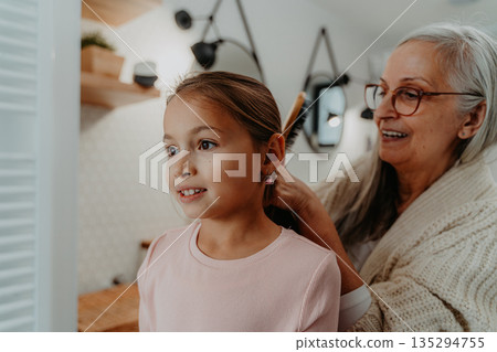 Grandmother making a ponytail to her granddaughter in bathroom in the morning. 135294755
