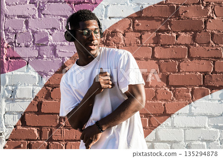 Man dancing with headphones against painted brick wall. Music enjoyment, personal freedom, and self expression through urban street culture 135294878