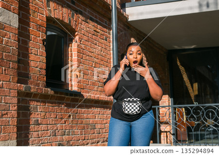 Woman reacting to phone call outside brick building. Surprise, emotional response, and real time communication through mobile technology and urban lifestyle Woman reacting to phone call outside brick building. Surprise, emotional response, and real time communication through mobile technology and urban lifestyle 135294894