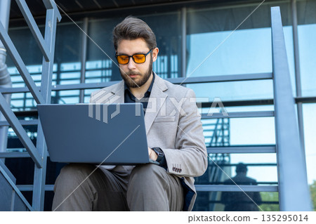 Professional man working on laptop in front of business center Professional man working on laptop in front of business center 135295014