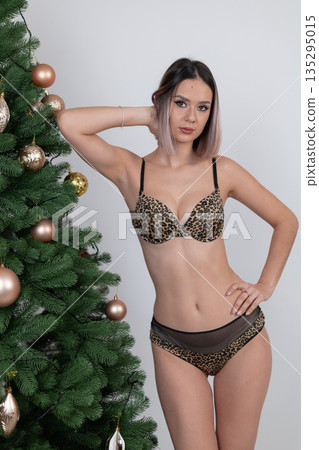 Woman in leopard lingerie leaning against Christmas tree 135295015