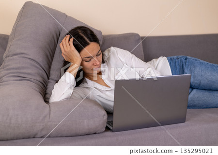 Tired woman lying on sofa with laptop working late Tired woman lying on sofa with laptop working late 135295021