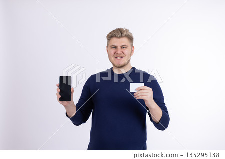Smiling man in blue sweater holding black smartphone 135295138