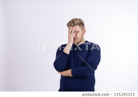 Man in dark blue sweater with hand on forehead Man in dark blue sweater with hand on forehead 135295153