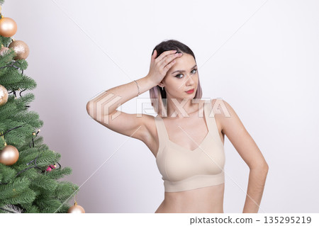 Woman in beige lingerie posing near Christmas tree 135295219