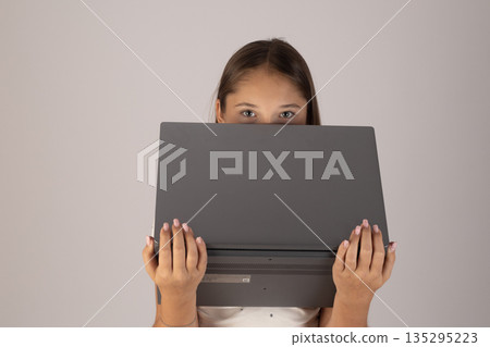 Young woman hiding face behind laptop screen 135295223