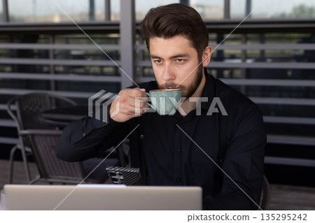 Man in black shirt drinking coffee at outdoor table 135295242