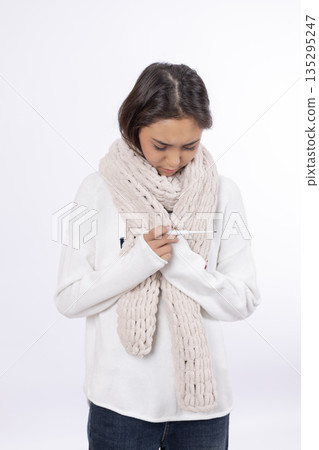 Sick woman in scarf checking thermometer Sick woman in scarf checking thermometer 135295247