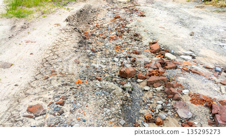 Old muddy country road with deep tire tracks and potholes left by rain, indicating poor condition 135295273