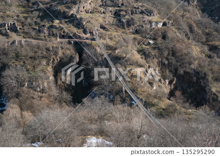 Abandoned cave dwellings, rugged hills in Khndzoresk, Armenia, with rocky textures, dry vegetation, suspension bridge crossing the gorge 135295290