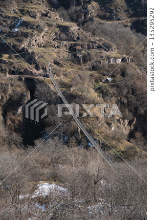 Abandoned cave dwellings, rugged hills in Khndzoresk, Armenia, with rocky textures, dry vegetation, suspension bridge crossing the gorge Abandoned cave dwellings, rugged hills in Khndzoresk, Armenia, with rocky textures, dry vegetation, suspension bridge crossing the gorge 135295292