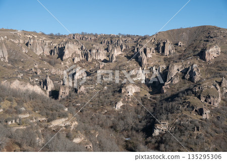 Rocky hills with caves and rugged cliffs in Khndzoresk, Armenia, under a clear blue sky, earthy tones and quiet natural atmosphere Rocky hills with caves and rugged cliffs in Khndzoresk, Armenia, under a clear blue sky, earthy tones and quiet natural atmosphere 135295306