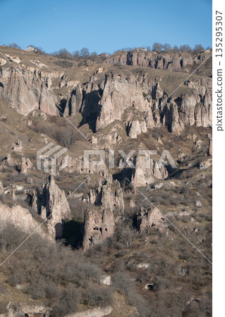 Rocky hills with caves and rugged cliffs in Khndzoresk, Armenia, under a clear blue sky, earthy tones and quiet natural atmosphere Rocky hills with caves and rugged cliffs in Khndzoresk, Armenia, under a clear blue sky, earthy tones and quiet natural atmosphere 135295307