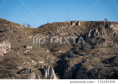 Rocky hills with caves and rugged cliffs in Khndzoresk, Armenia, under a clear blue sky, earthy tones and quiet natural atmosphere 135295309