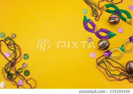 Mardi gras carnival masks, beads, and doubloons on yellow surface Mardi gras carnival masks, beads, and doubloons on yellow surface 135295430