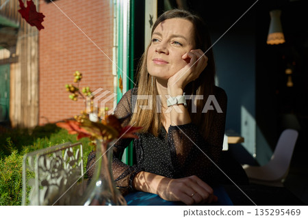 Woman sitting by window in cafe looking into sunlight Woman sitting by window in cafe looking into sunlight 135295469