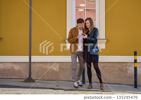 Couple looking at smartphone near yellow building wall Couple looking at smartphone near yellow building wall 135295470