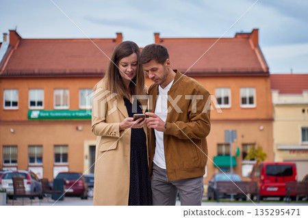 Man and woman checking smartphone while standing in city center Man and woman checking smartphone while standing in city center 135295471