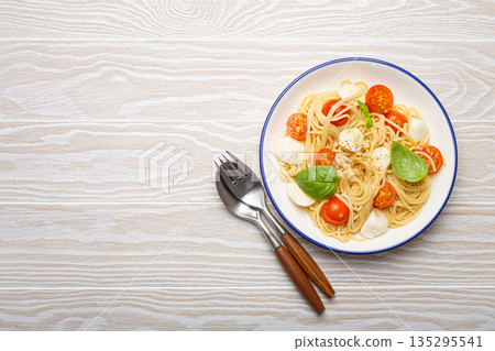Plate of spaghetti pasta with cherry tomatoes and mozzarella cheese on white wooden background with copy space Plate of spaghetti pasta with cherry tomatoes and mozzarella cheese on white wooden background with copy space 135295541