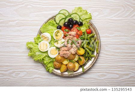 Nicoise salad with tuna, eggs, potatoes, green beans, and olives on a white table Nicoise salad with tuna, eggs, potatoes, green beans, and olives on a white table 135295543