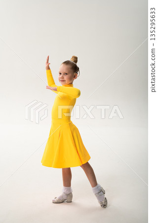 Little girl in yellow dress dancing with cochlear implant. Overcoming hearing loss through rhythm, art, inclusion, and strength of spirit in artistic gymnastics and ballroom dance. 135295633
