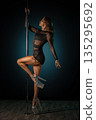 Graceful performer frozen in motion. Choreographed pole dance pose captured in sophisticated studio setting turned striking portrait 135295692